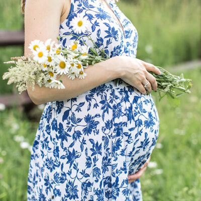 image of belly of pregnant woman holding daisies in a field